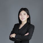 Studio shot of a woman in a black suit posing confidently against a gray background.