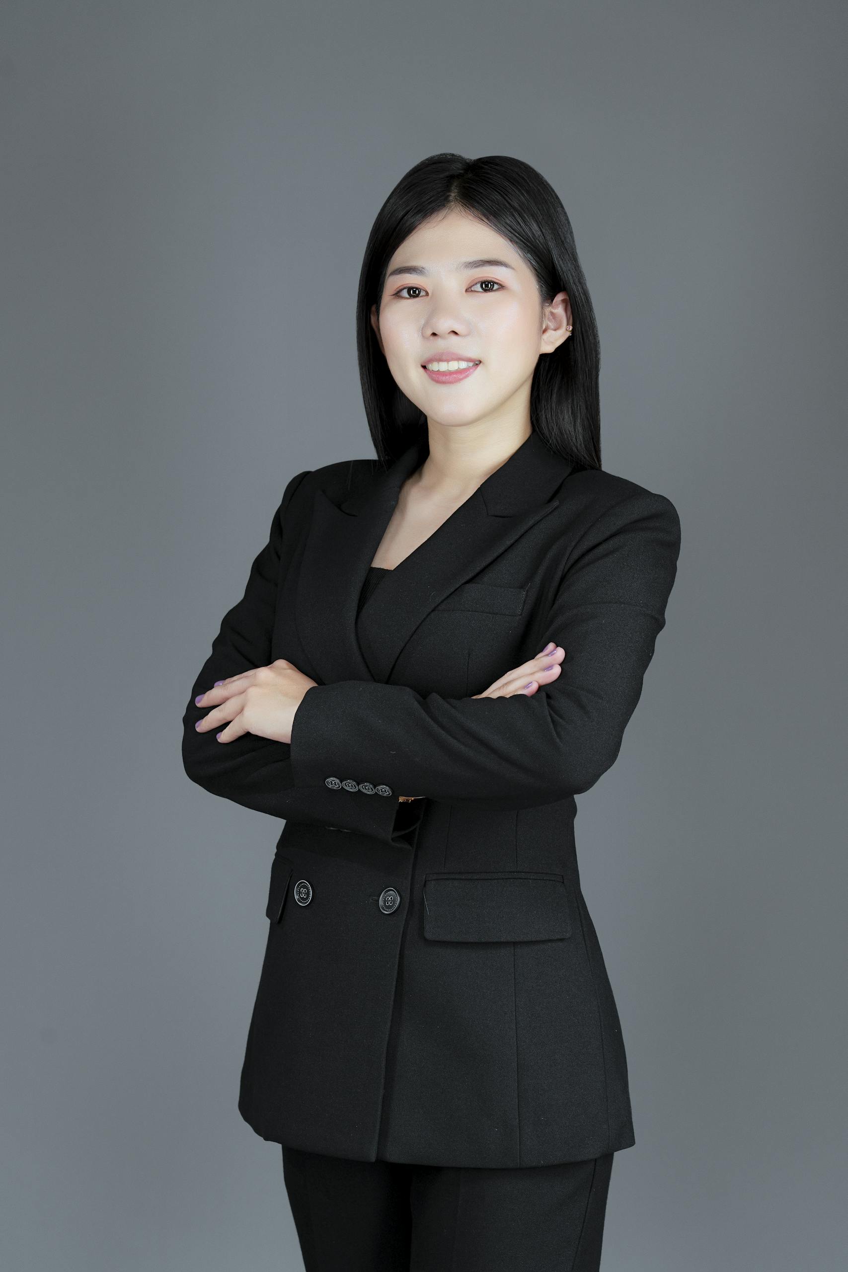 Studio shot of a woman in a black suit posing confidently against a gray background.